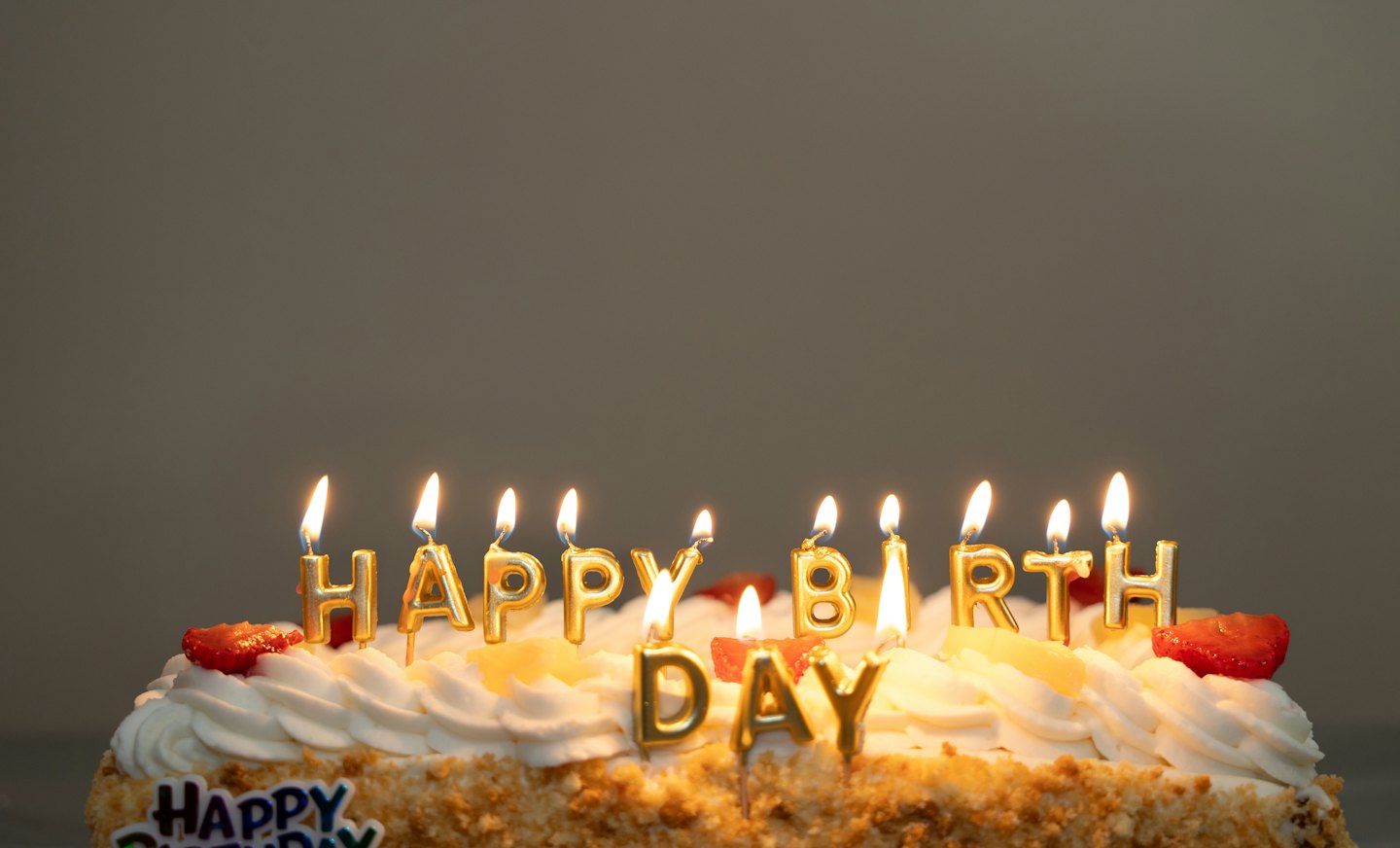 Frosted birthday cake with lit candles and fruit.