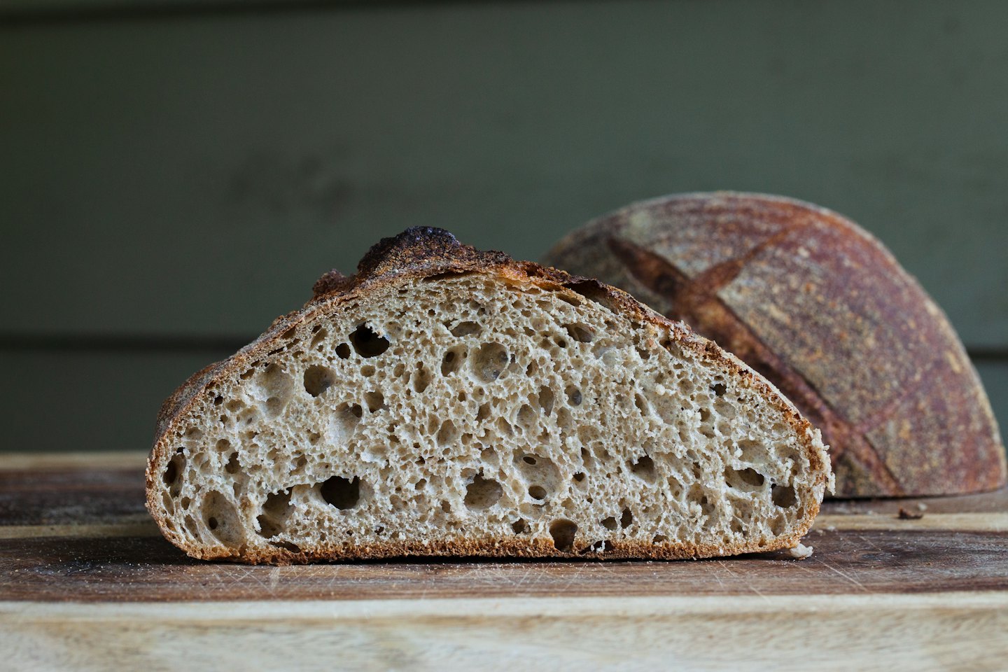 Sliced sourdough bread with a porous crumb on a wooden board.